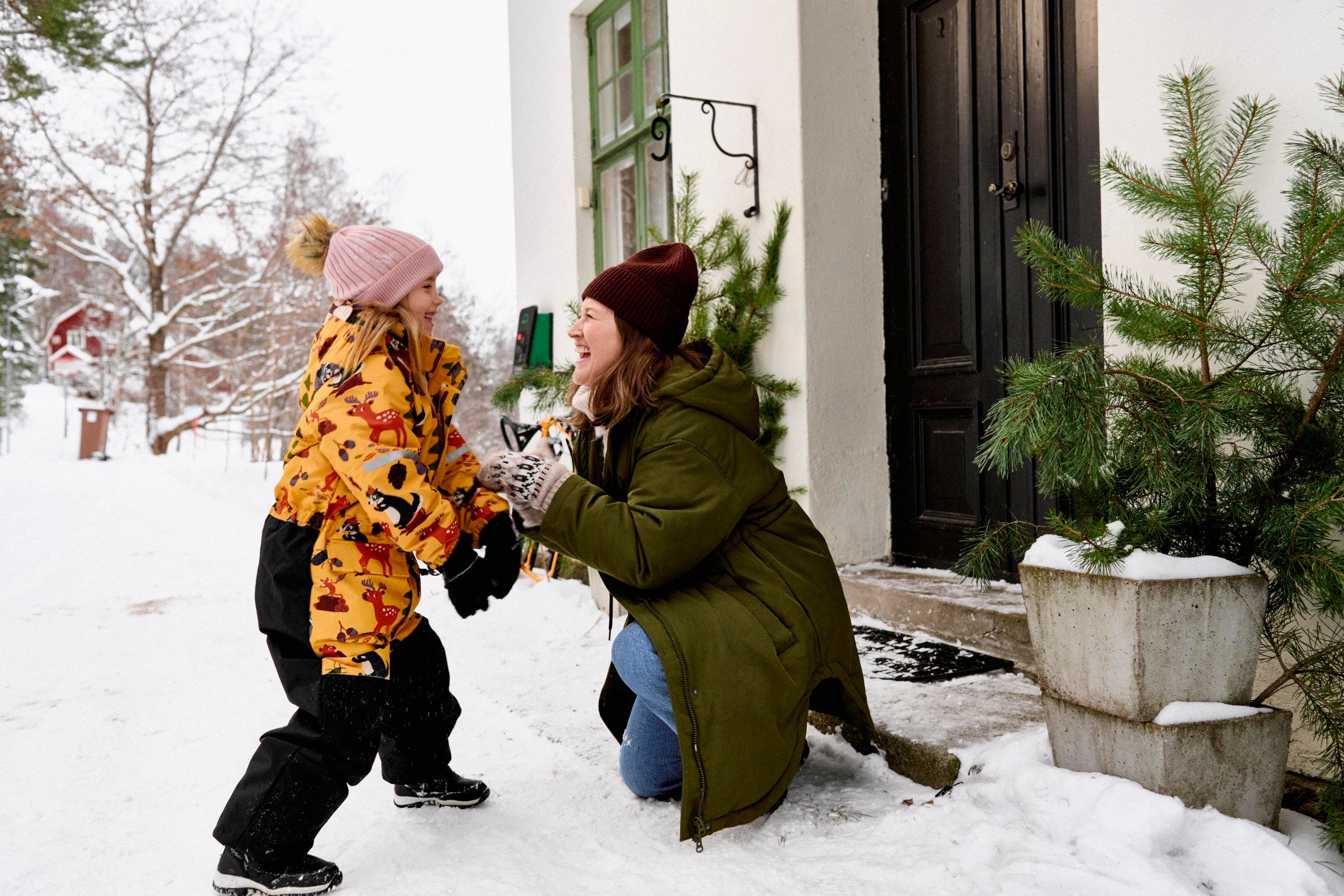 En kvinna och ett barn skojar i snön utanför ett hus